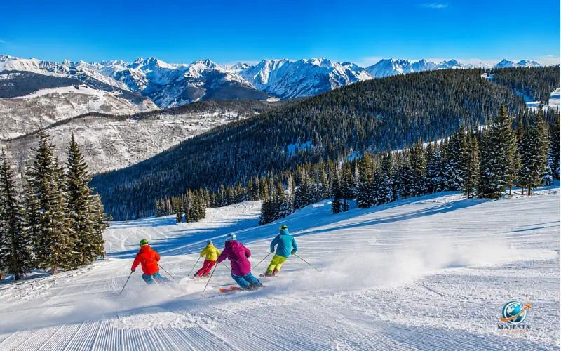 Skiers enjoying a sunny day on snow-covered slopes with panoramic Rocky Mountain views in Vail, Colorado. 
